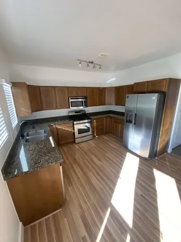 Kitchen featuring wood-finish flooring, stainless steel appliances, granite countertops, and wood cabinetry