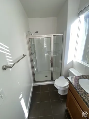 Enclosed shower with glass doors, dark tile flooring, vanity with an integrated sink, and a stone-look countertop
