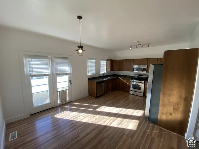 Open-concept kitchen and dining area featuring wood-finish flooring, stainless steel appliances, dark countertops, and wood cabinetry
