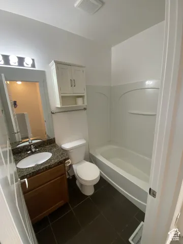Bathroom featuring a white bathtub, dark tile flooring, vanity with a rectangular sink, and an overhead vanity light fixture