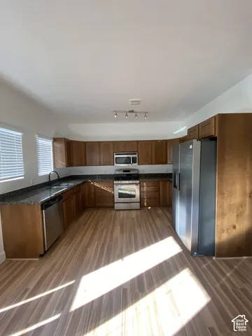Kitchen featuring wood-finish flooring, granite-style countertops, wood cabinetry, stainless steel appliances, and a track lighting fixture