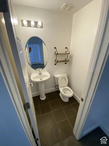 Pedestal sink, wall-mounted oval mirror, three-bulb vanity light fixture, toilet, and square floor tiles