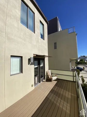 Private outdoor deck featuring composite decking, a metal and translucent panel railing, and stucco exterior walls