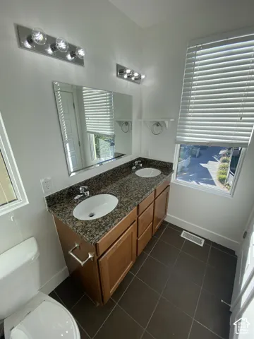 Dual vanity with integrated sinks, wood-finish cabinetry, and a stone countertop
