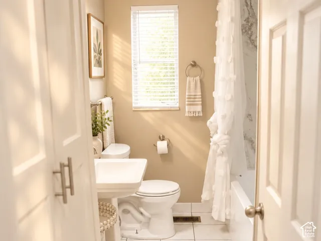 Pedestal sink, white tile flooring, built-in storage cabinet, window with blinds, and a shower-over-tub combination with a paneled surround