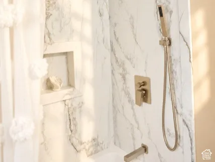 Tub/shower combination featuring marbled wall surrounds, a built-in shower niche, and brushed nickel fixtures including a rainfall shower head and a handheld shower head