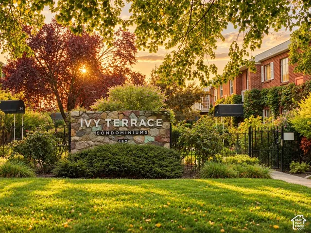 Stone-clad entrance signage, lush landscaping, wrought iron fencing, brick exterior, and mature trees