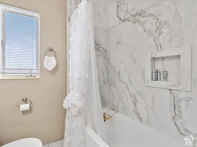 Bathtub featuring marble-look wall tiling and a built-in shower niche