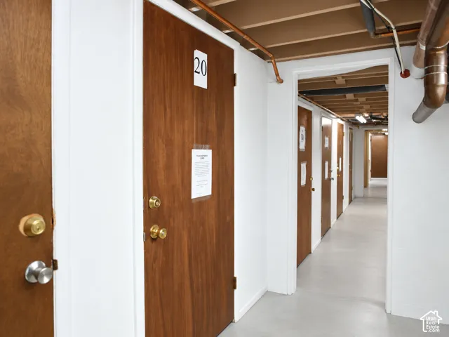 Hallway with multiple wood-paneled doors, exposed ceiling joists, and concrete flooring