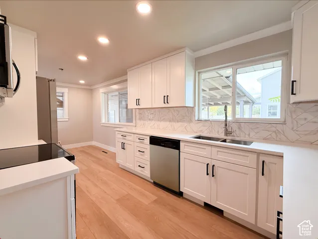Kitchen featuring light wood-finish flooring, white shaker cabinetry, white countertops, a stainless steel double basin sink, and a patterned backsplash