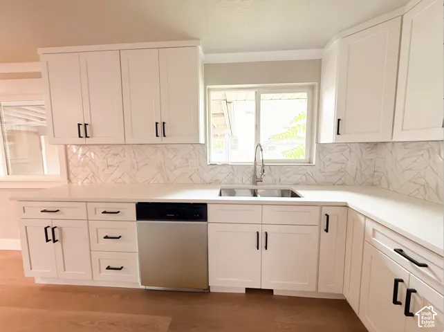 White shaker-style cabinetry with matte black hardware, solid surface countertops, patterned tile backsplash, and a stainless steel dishwasher