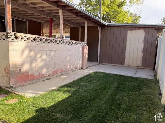 Covered patio with decorative block wall, concrete walkway, and adjacent storage shed