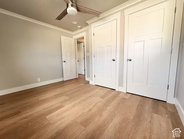 Wood-finish flooring, white trim, crown molding, two panel doors, and a ceiling fan with integrated lighting