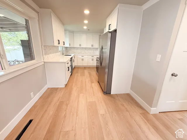 Kitchen featuring wood-finish flooring, white cabinetry with dark hardware, a light-toned backsplash, stainless steel appliances, and recessed lighting
