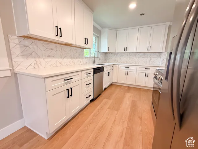 White shaker cabinetry, light-toned wood-finish flooring, white countertops, patterned backsplash, and stainless steel appliances