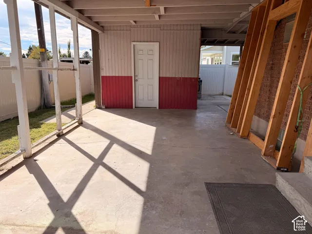 Covered patio area with a concrete surface, white paneled walls, and a white exterior door