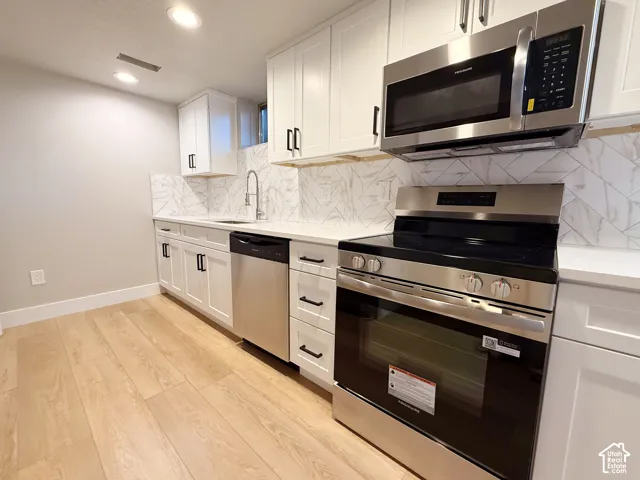 Kitchen featuring white shaker cabinetry, stainless steel appliances, light-toned wood-finish flooring, white countertops, and a patterned backsplash