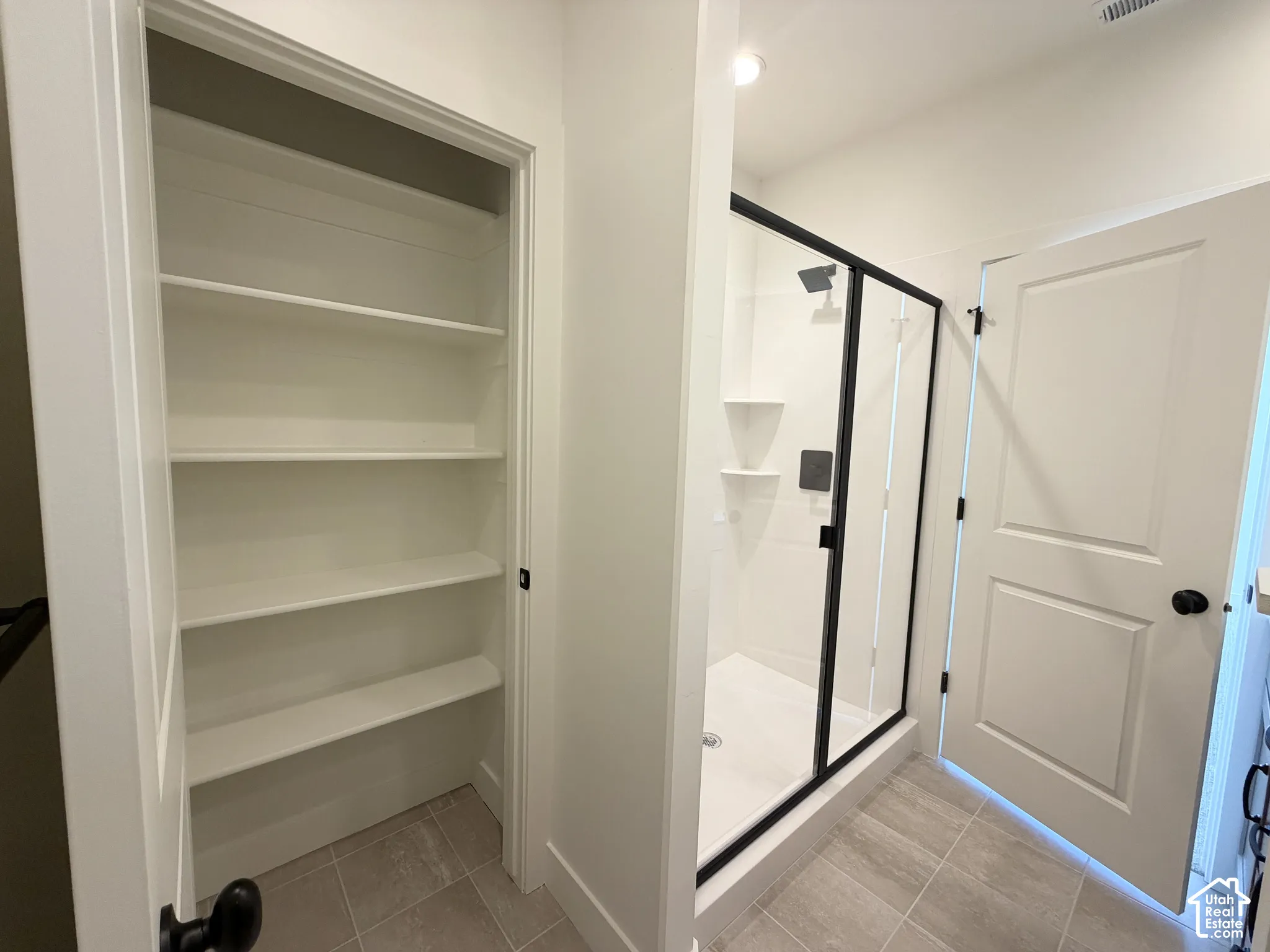 Built-in shelving, glass-enclosed shower with matte black fixtures, tile flooring, white interior doors