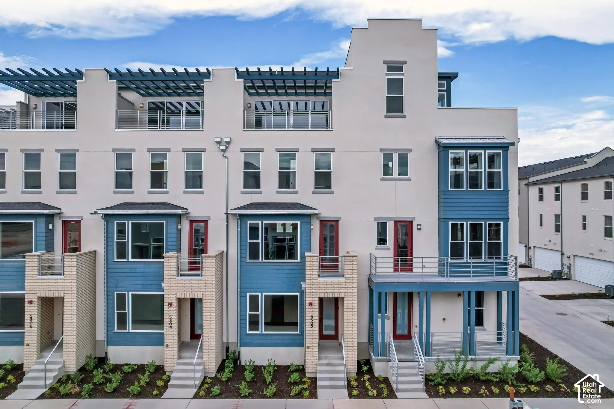 Contemporary multi-level townhome featuring a stucco and siding exterior, multiple balconies, and a pergola-covered rooftop deck
