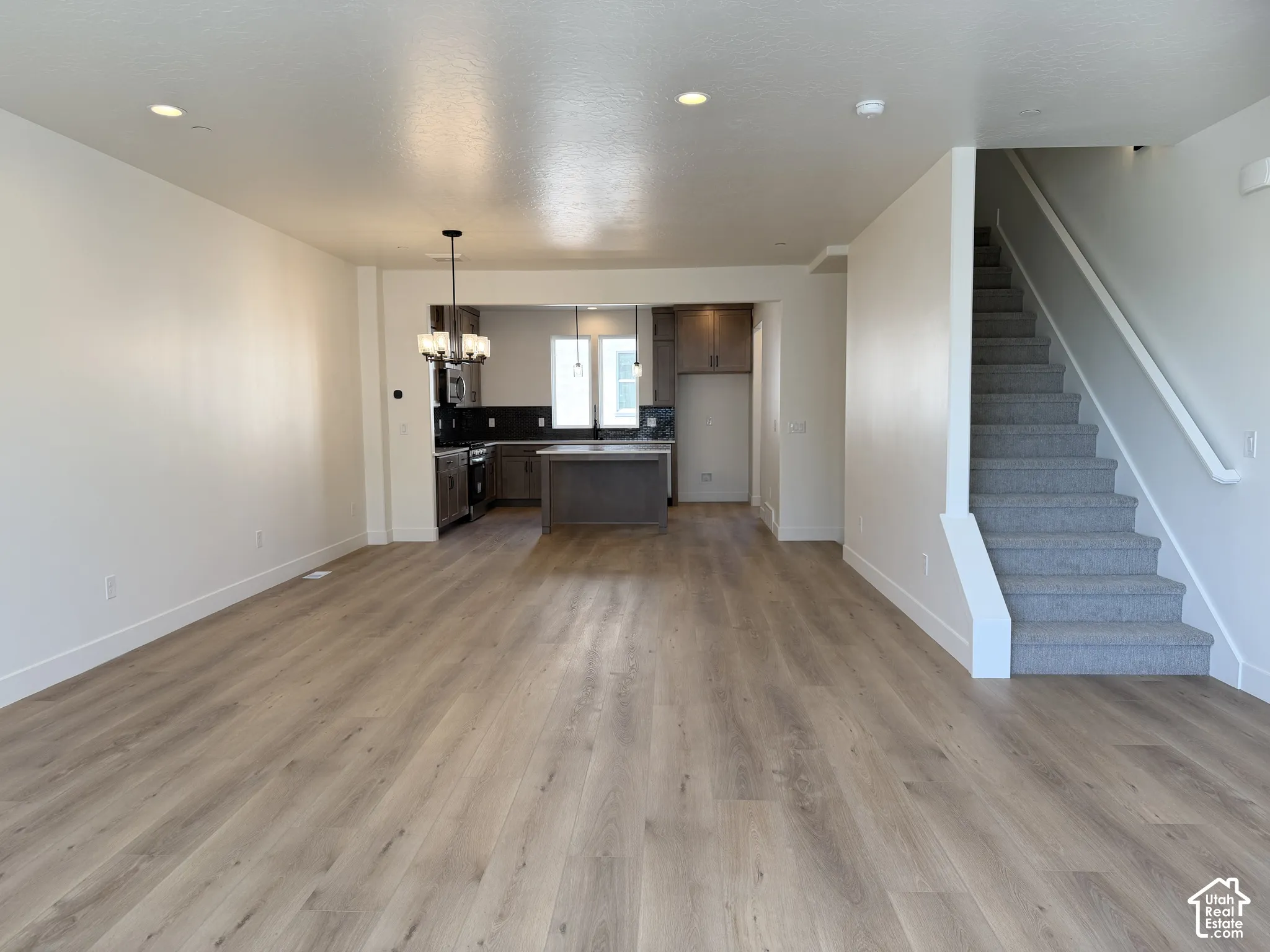 Open-concept living area featuring wood-finish flooring, recessed lighting, and a kitchen with an island, dark cabinetry, and pendant lighting