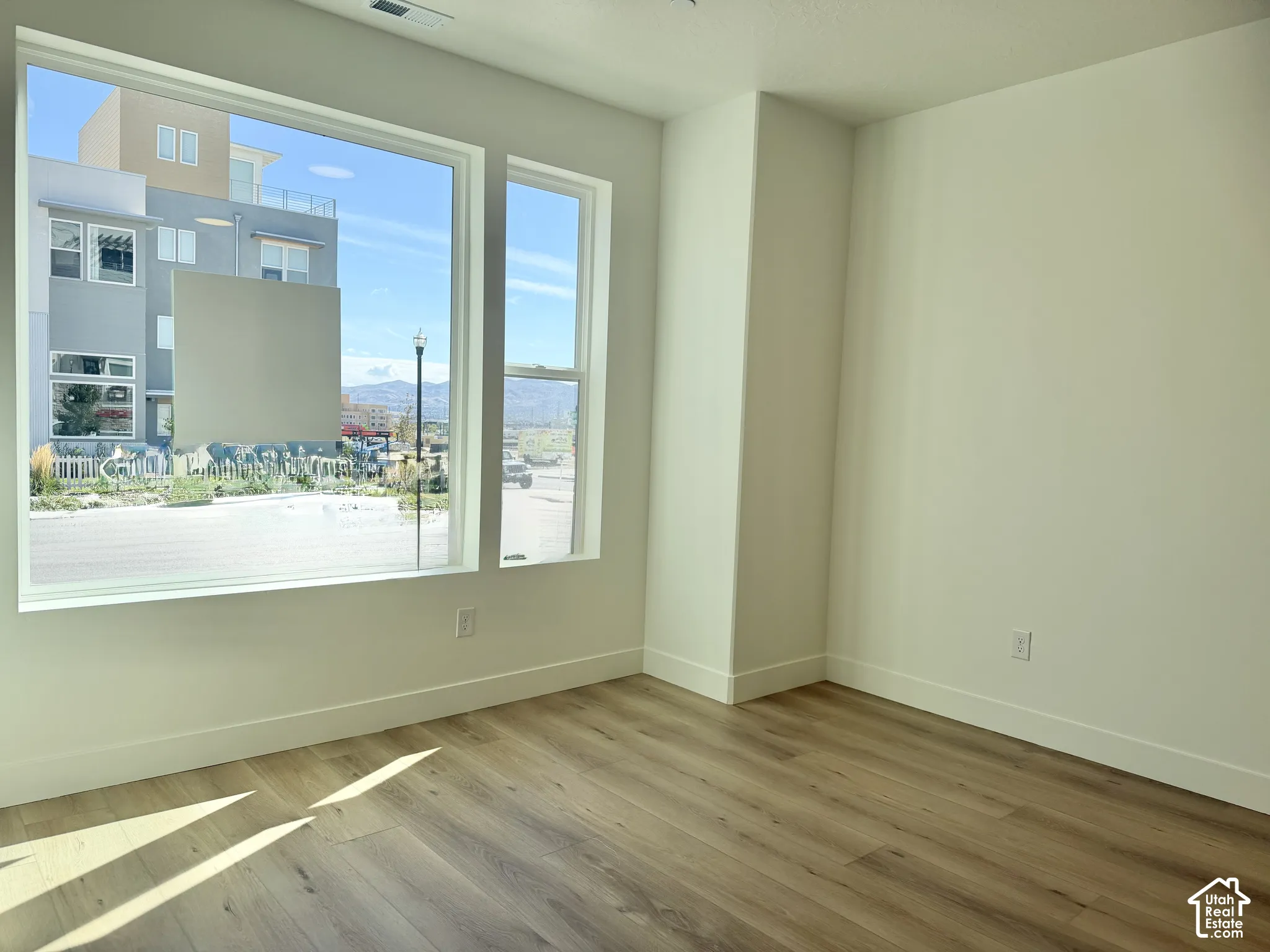 Expansive room with wood-finish flooring, white walls, and large windows