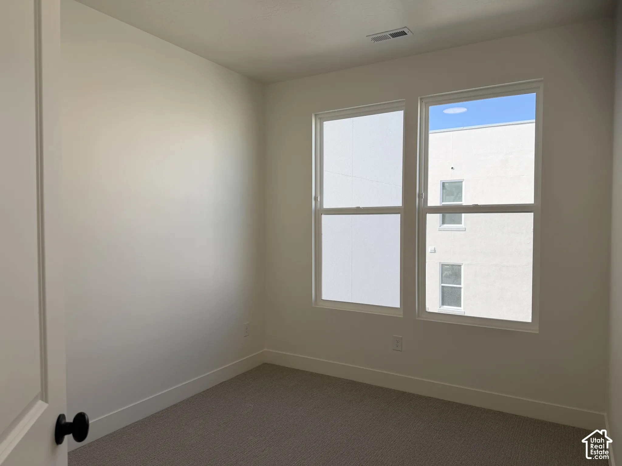 Dual pane windows provide ample natural light within this room, featuring light neutral wall tones and a textured carpet flooring