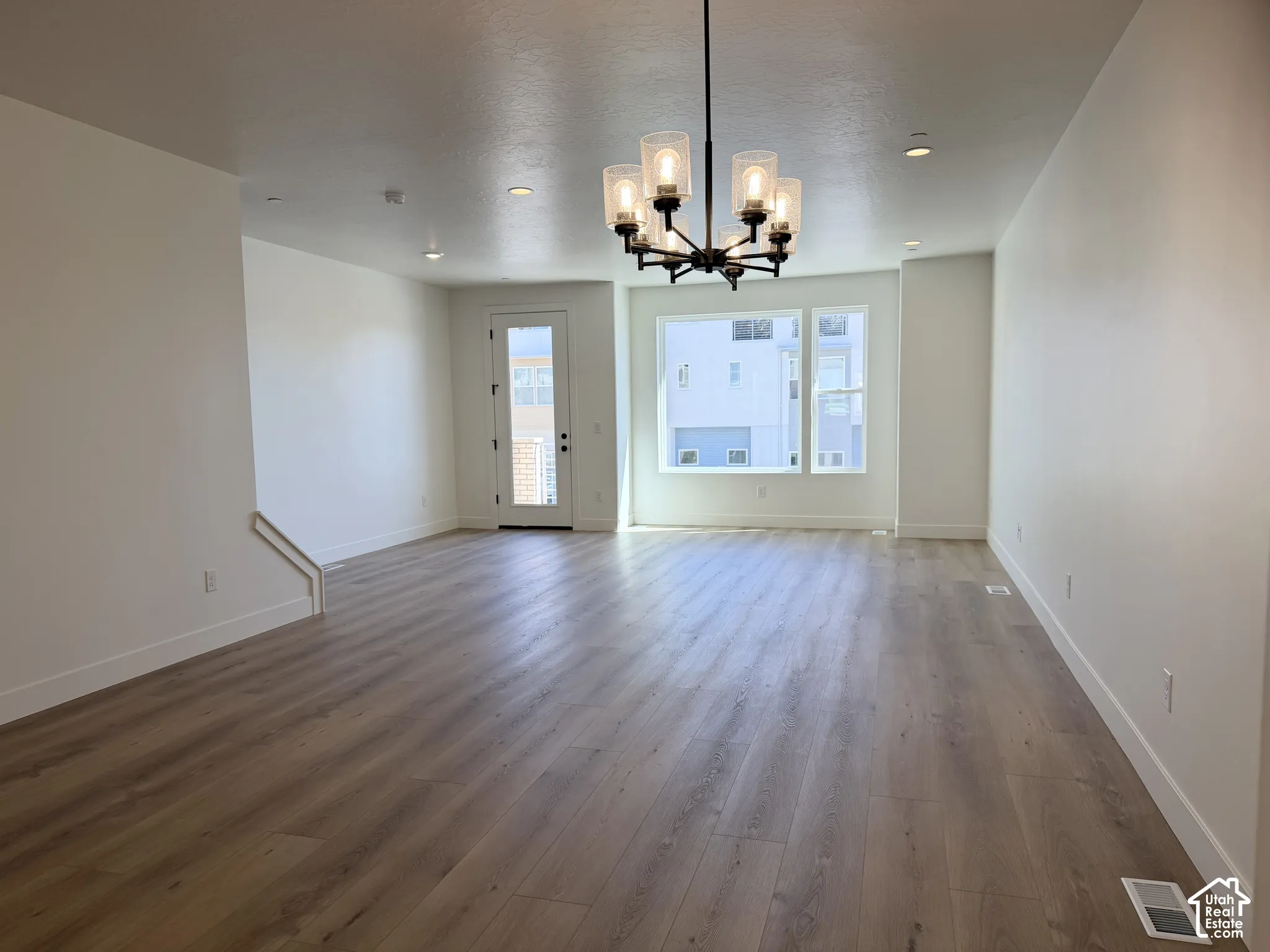 Spacious living area featuring wood-finish flooring, a modern chandelier, recessed lighting, and large windows