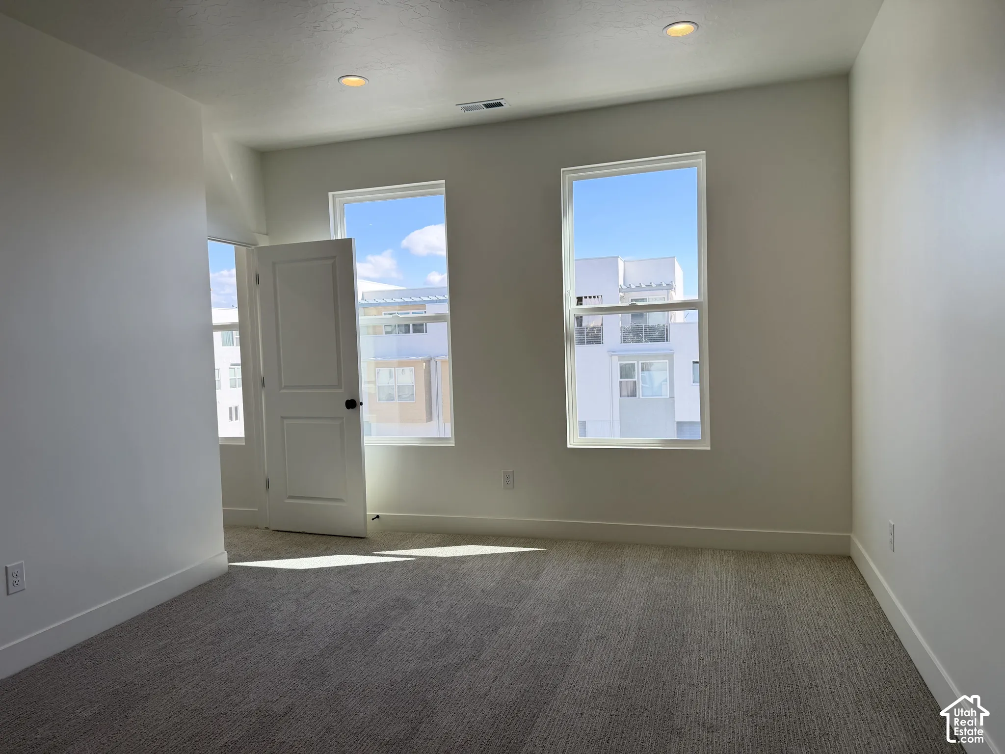 Carpeted flooring with white walls, two recessed lights, and two double-hung windows