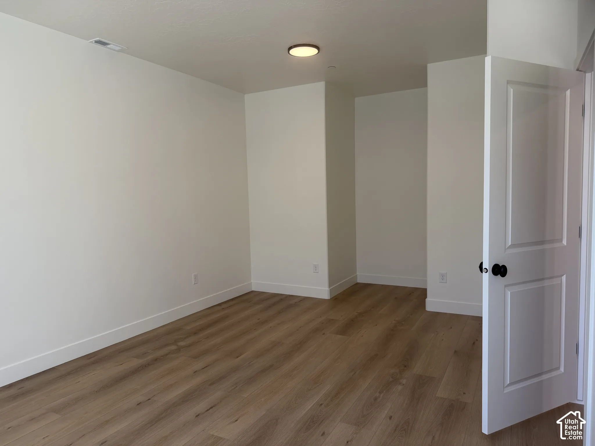 Wood-finish flooring, white walls, white trim, and a white interior door with black hardware