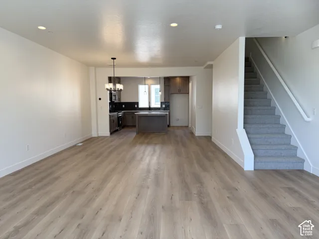 Open-concept living area featuring wood-finish flooring, recessed lighting, and a kitchen with an island, dark cabinetry, and pendant lighting
