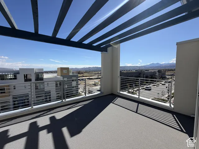 Expansive outdoor terrace featuring a textured gray surface, a slatted pergola, and metal railings