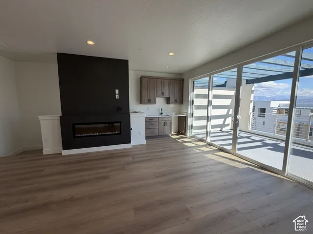 Wood-finish flooring throughout, integrated electric fireplace, recessed lighting, built-in wet bar, and expansive sliding glass doors leading to an exterior balcony