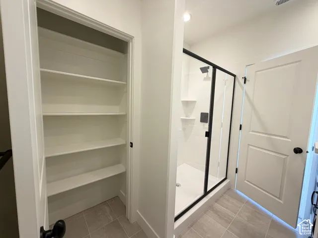 Built-in shelving, glass-enclosed shower with matte black fixtures, tile flooring, white interior doors