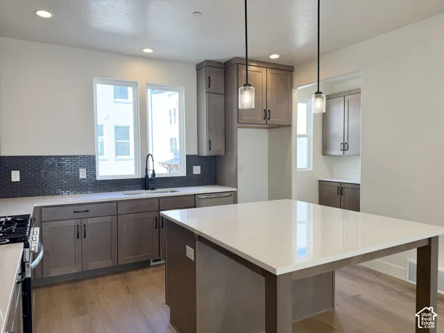 Kitchen featuring a large island with a light-colored countertop, wood-finish flooring, dark subway tile backsplash, and shaker-style cabinetry with dark hardware