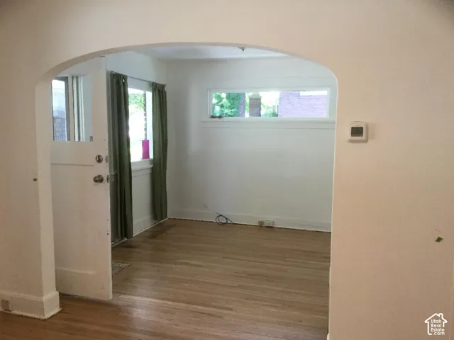 Arched entryway leading to a room with wood-finish flooring, white walls, and a window with a deep sill
