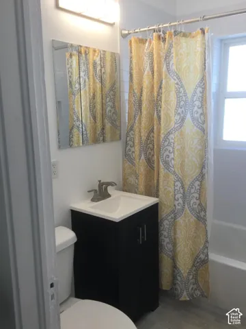 White subway tile shower surround, window, light wood-finish flooring, dark wood vanity with integrated sink, and brushed nickel faucet