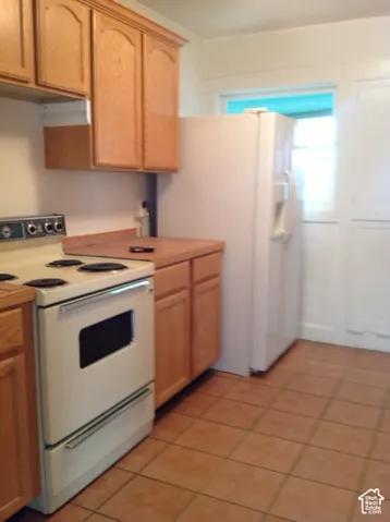 Wood-finish cabinetry, tile flooring, and integrated white appliances