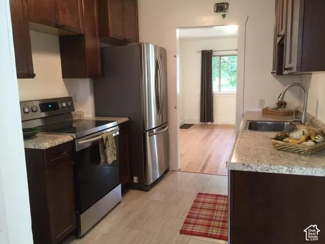 Kitchen featuring dark wood cabinetry, light speckled countertops, stainless steel appliances, a stainless steel sink with a high-arch faucet, and light tile flooring