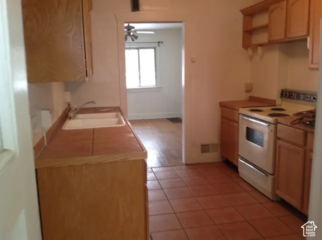 Kitchen featuring tiled flooring, wood-finish cabinetry, a double basin sink, and a freestanding electric range