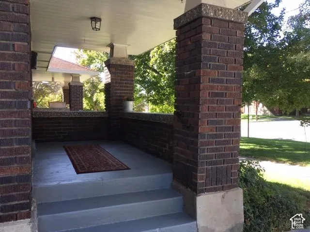 Brick porch columns featuring stone caps, a painted concrete floor, and a built-in wall light fixture