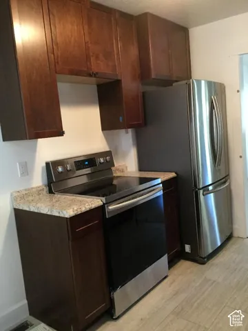 Dark wood cabinetry, speckled countertops, stainless steel electric range, and a stainless steel refrigerator