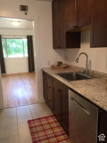 Kitchen featuring dark wood-finish cabinetry, light-toned countertops, and a stainless steel dishwasher