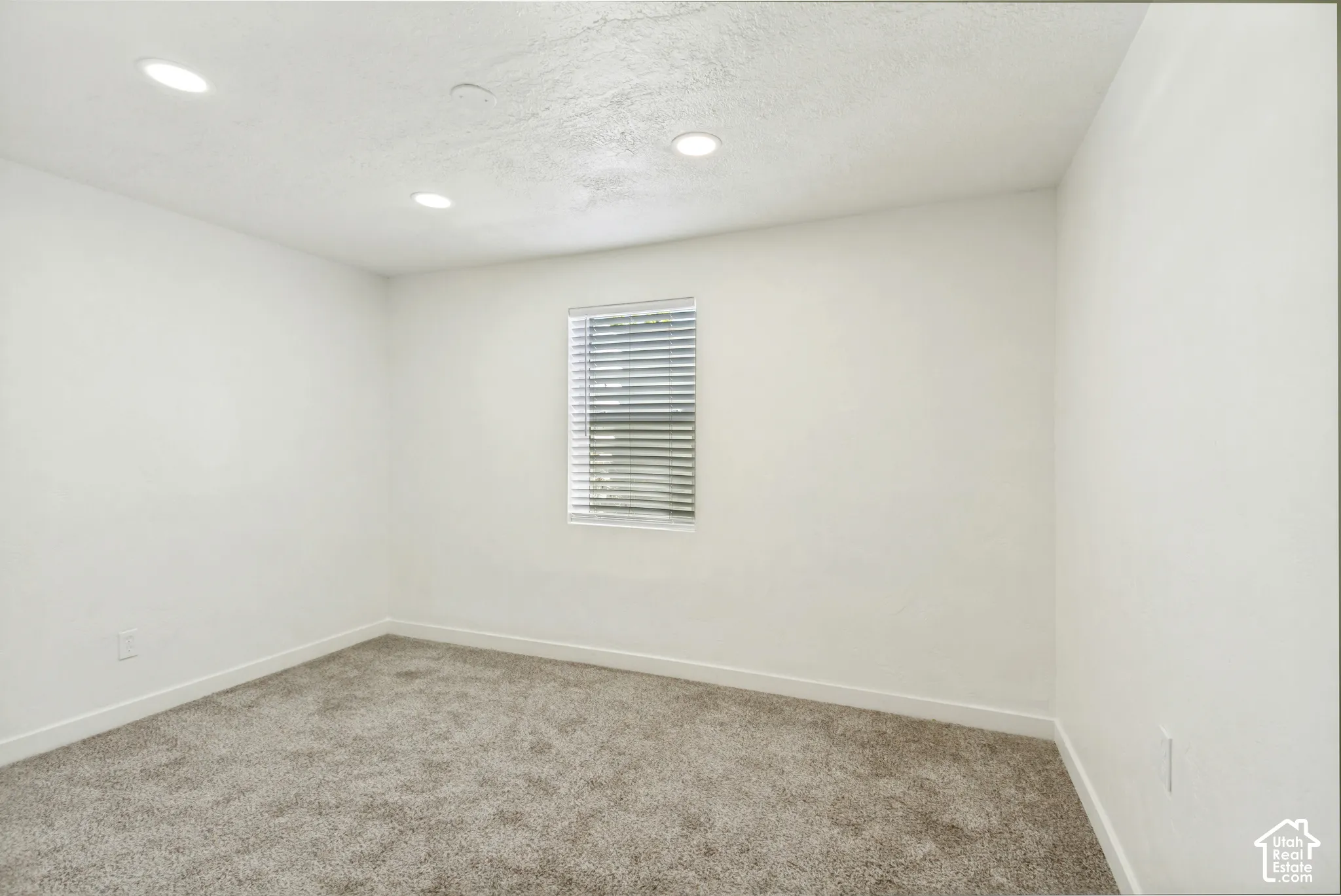 Neutral-toned walls, recessed ceiling lighting, textured ceiling, and a window with horizontal blinds