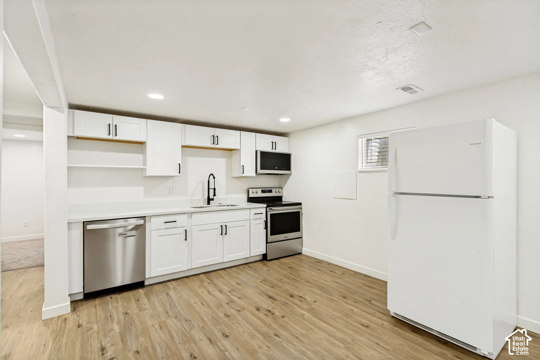 Kitchen featuring wood-finish flooring, white cabinetry, a stainless steel dishwasher, a stainless steel range, and an over-the-range microwave