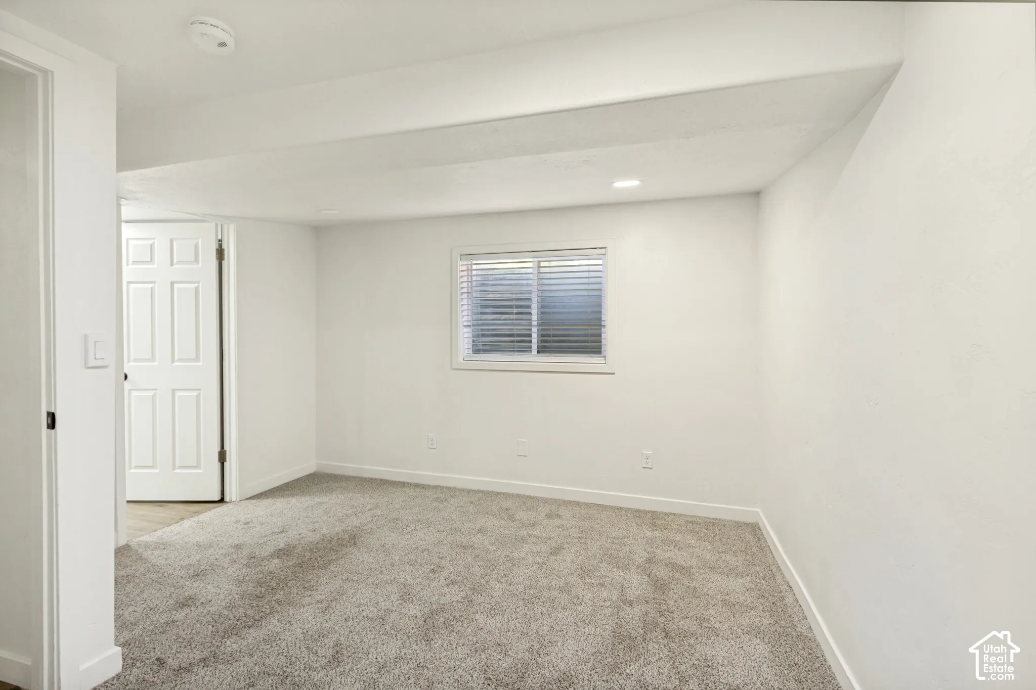 Recessed lighting, light gray carpeting, white walls, and a multi-pane window with blinds