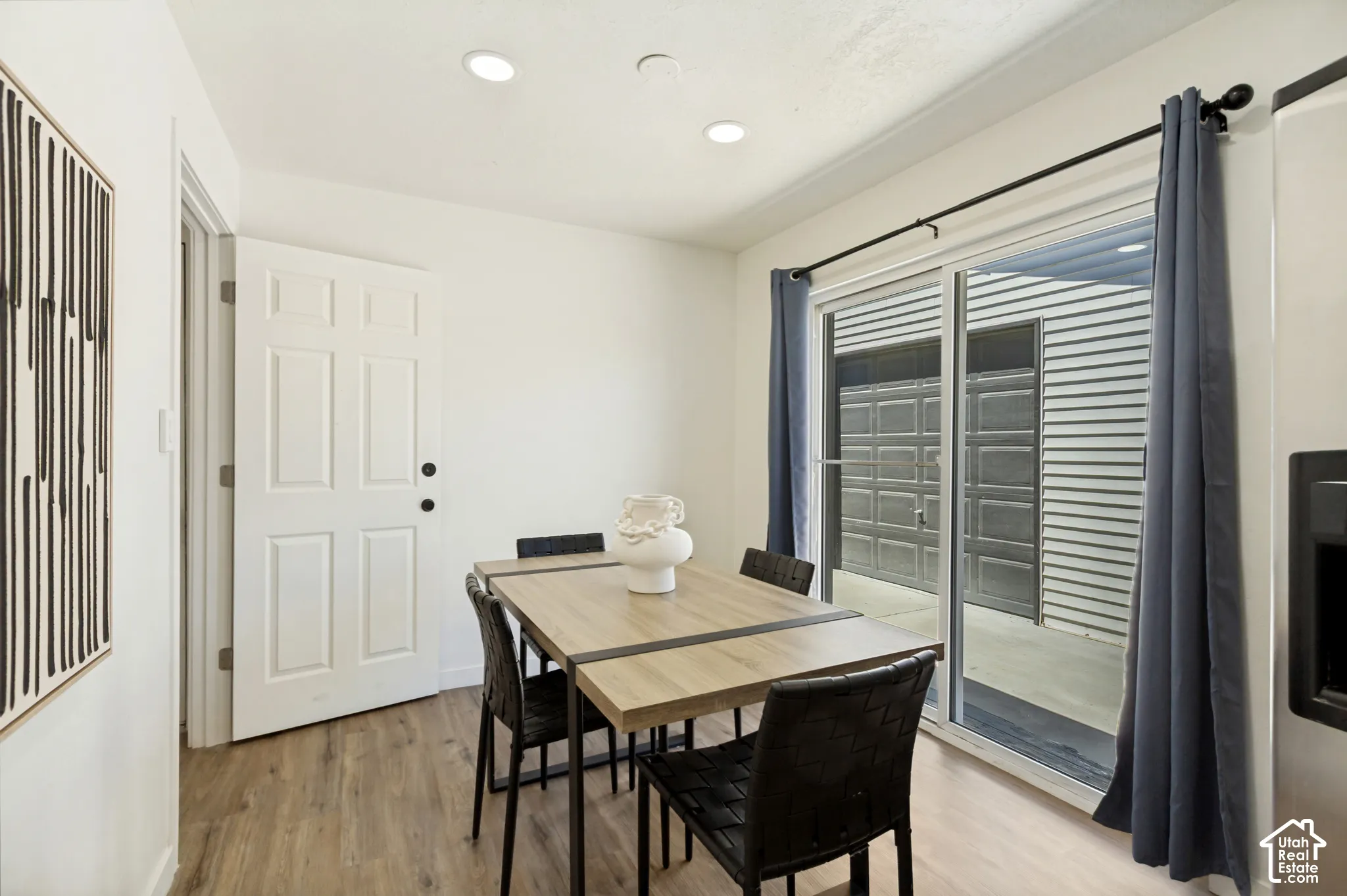 Recessed ceiling lighting, wood-finish flooring, white paneled door, and a sliding glass door
