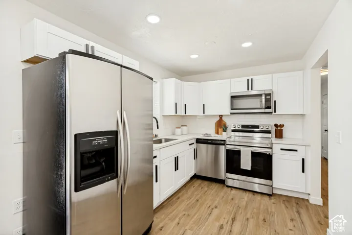 Kitchen featuring white cabinetry, stainless steel appliances, recessed lighting, wood-finish flooring, and a subway tile backsplash