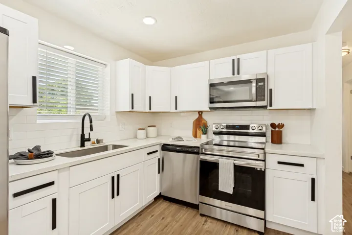 White shaker-style cabinetry with matte black hardware, stainless steel appliances, durable wood-finish flooring, white subway tile backsplash, and recessed lighting