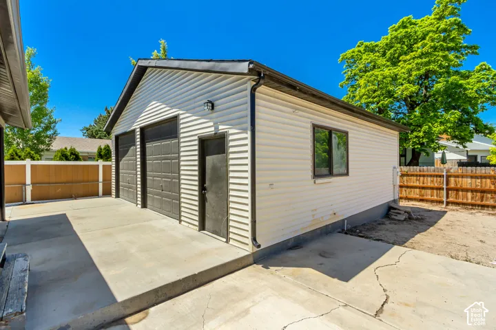 Detached two-car garage with white vinyl siding, two dark paneled garage doors, and a side entry door