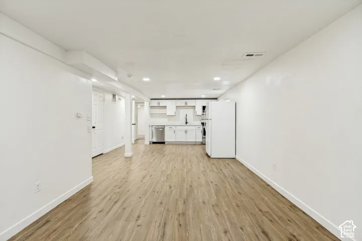 Wood-finish flooring throughout, recessed lighting, white cabinetry, stainless steel dishwasher, and a black faucet
